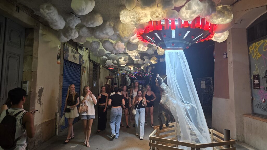 Decorated street with UFO and lights at Las Fiestas de Gràcia 2025 in Barcelona, people enjoying the festival atmosphere