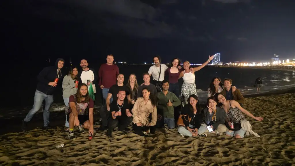 International friends celebrating the second night of La Mercè Festival 2025 at Bogatell Beach in Barcelona, with the skyline and sea at night.